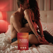 A couple in their forties on the bed, her wrists in handcuffs as he kisses her, a pouch of Moodie Desire Gummies in front